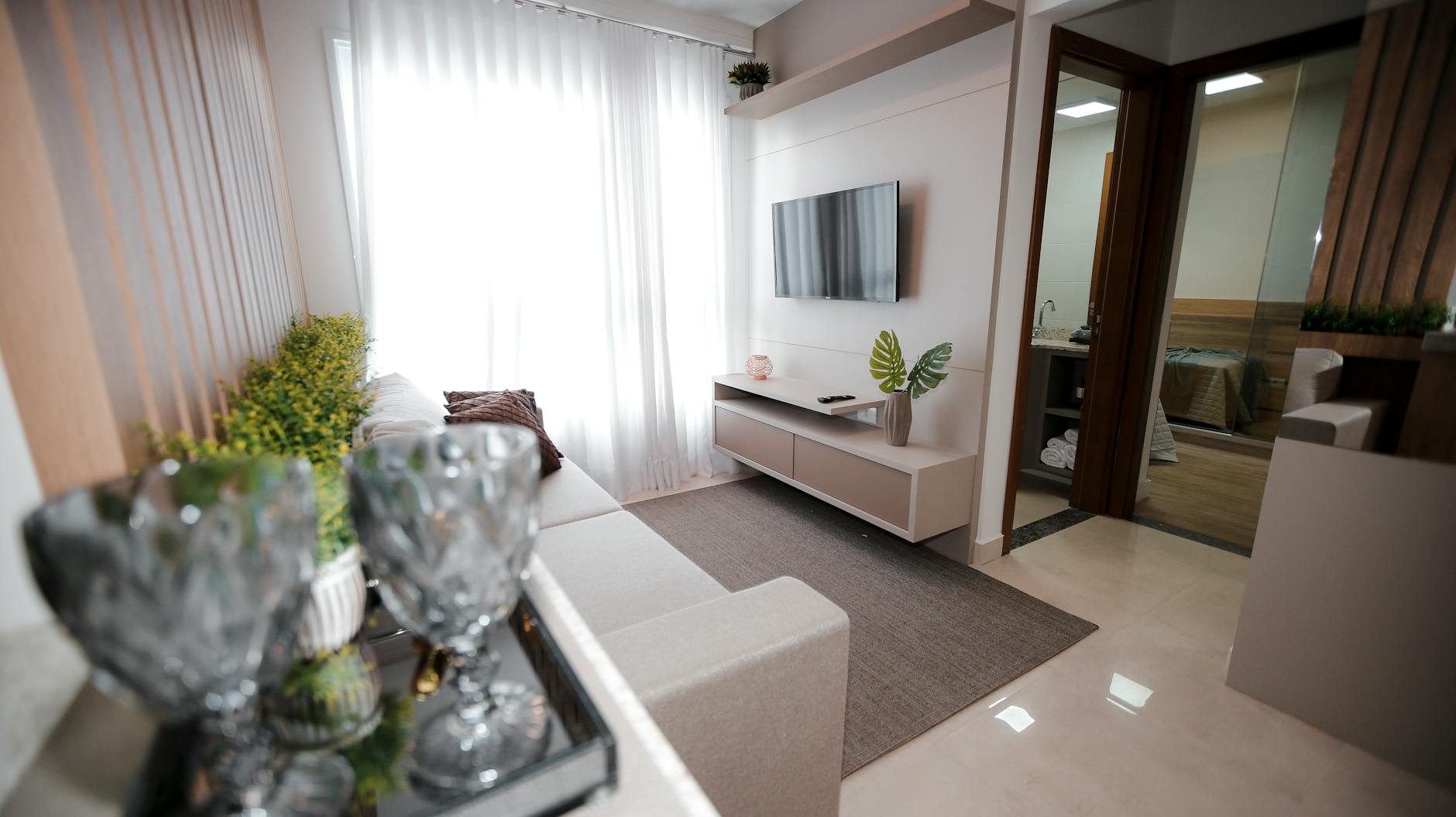 Jasny wąski salon z minimalistycznymi meblami, TV na ścianie i roślinami