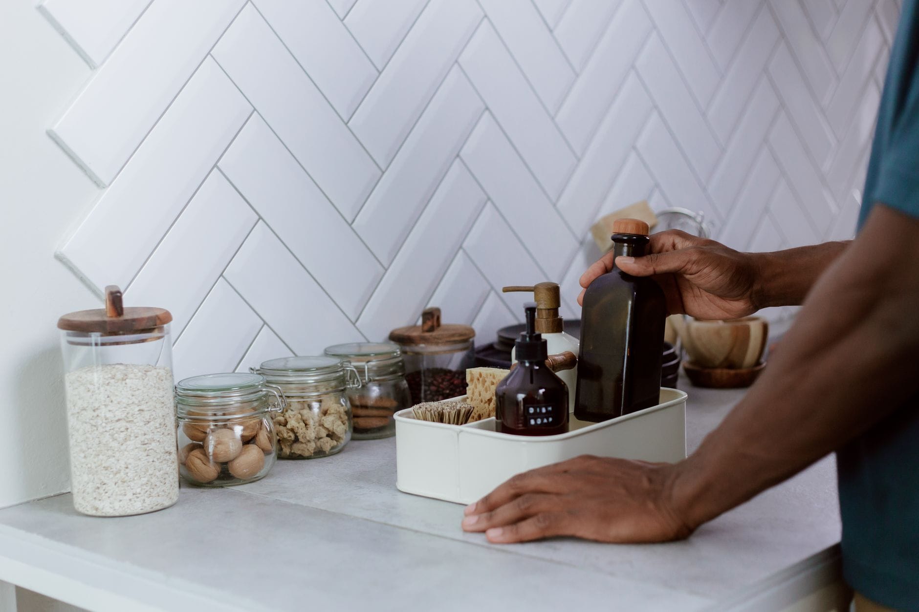 Jak zorganizować kuchnię zero waste: praktyczne wskazówki dla początkujących Osoba porządkuje kuchenny blat, ustawiając szklane słoiki wielokrotnego użytku